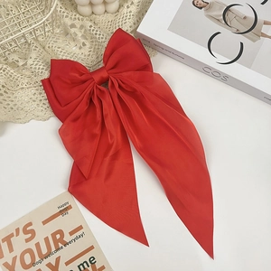 Detail of red oversized satin bow hair clip with long ribbons on a decorative lace background