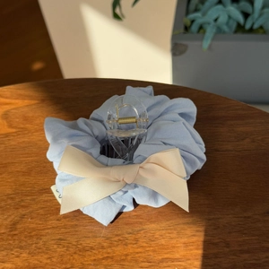 Macro shot of light blue scrunchie with cream ribbon bow and clear hair claw clip