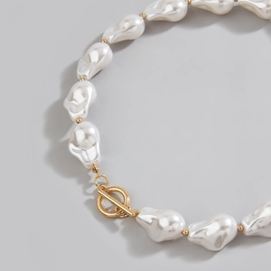 Detailed close-up of Baroque pearl necklace with gold T-bar clasp and metallic spacers