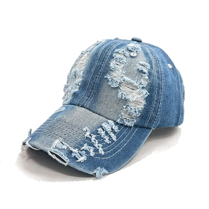 Detail showing distressed holes and white stitching on washed blue denim baseball cap