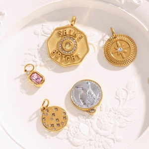 Detailed view of 18K gold plated charms with crystals and Queen coin pendant on a white plate
