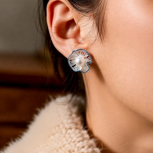 Close-up of a hollow pearl flower earring worn by a model in a warm elegant setting