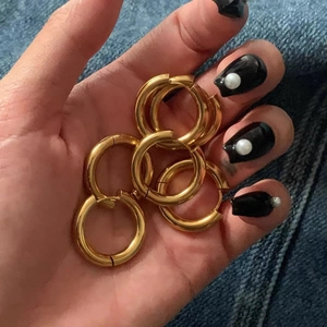 Detailed close-up of three pairs of chunky gold double-hoop earrings held in palm