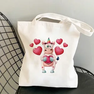White canvas tote bag featuring a colorful cartoon unicorn and red heart print on a chair