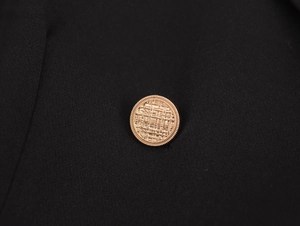 Detailed close-up of a golden woven texture metal button on a black coat