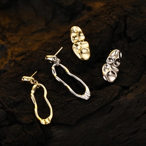 Asymmetric lava liquid metal drop earrings in gold and silver finish on black wood