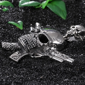Macro detail of stainless steel skull pendant with twin pistols on black sand base