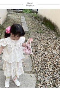 Pink drawstring bag with pearl handle and frilled details on a young girl's white outfit