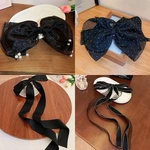 Detail view of four black mesh bow hair clips with pearls and ribbons on wooden surface