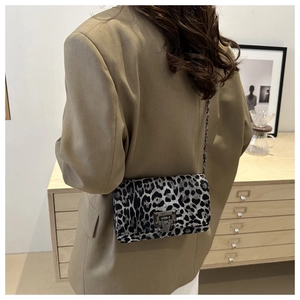 Detail of leopard print bag with metal chain strap worn by model in minimalist setting