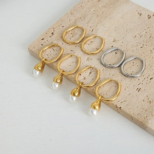 Elegant gold oval hoop earrings with white pearl pendants on a beige stone background