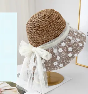 Detail of floral lace embroidery and large white mesh bow on a woven summer straw hat