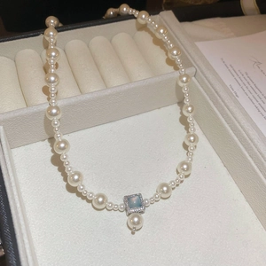 Close-up of pearl necklace featuring a square blue stone pendant in a jewelry box