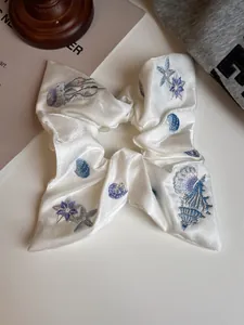 Detail view of premium satin scrunchie with intricate ocean sea shell embroidery