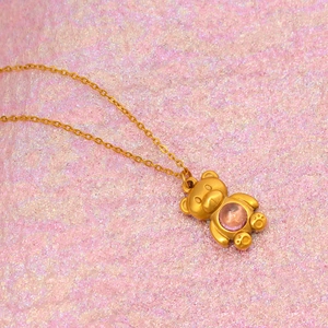 Golden bear pendant necklace with purple gemstone on a romantic pink glitter background
