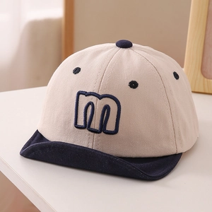 Detail of baby soft brim cap showing navy blue letter m embroidery on beige cotton fabric