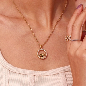 Detail of 18K gold-plated Evil Eye heart necklace worn by a model on beige knitwear