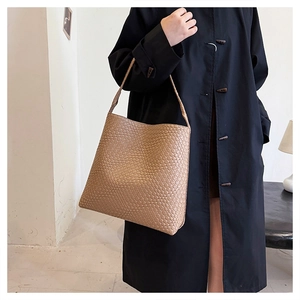 Detailed view of camel woven faux leather shoulder bag styled with a black trench coat