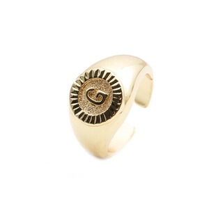 Detailed close-up of golden metal open ring featuring a round face with embossed letter G