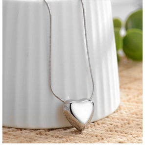 Polished silver heart pendant necklace on snake chain displayed on white ceramic