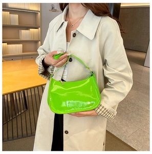 Neon green glossy patent leather baguette bag with gold zipper held by a model