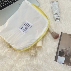 Close-up of a white waterproof makeup bag with yellow zipper on a plush white surface