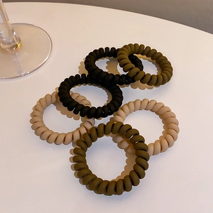 Detail of 6 matte spiral hair ties in earthy tones stacked on a white surface