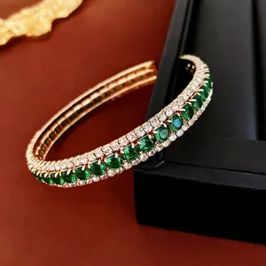 Elegant gold open bangle featuring green emerald-cut stones and white zircon accents