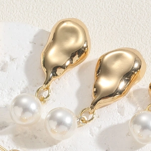 Macro detail of gold-tone geometric earring with white pearl on white stone texture