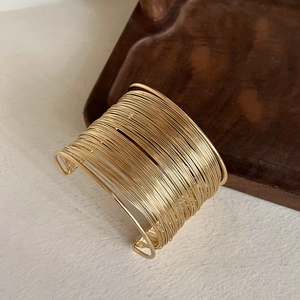 Detailed view of wide irregular gold wire cuff bracelet on a wooden tray