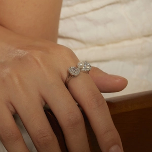 Macro shot of silver ring with two heart-shaped zircons and a white pearl on a model finger