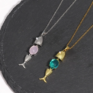 Detail view of moving fish pendants with colorful gems and pearls on textured slate