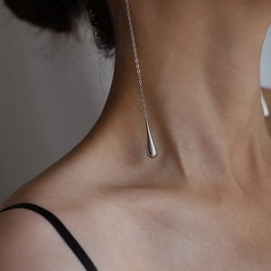 Macro detail of polished silver teardrop earring with long elegant chain tassel