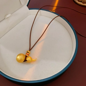 Detail of brushed gold gourd pendant on brown woven cord inside a white jewelry box
