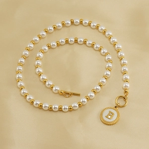 Close-up of pearl necklace with gold letter B pendant on champagne satin background