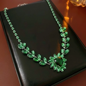 Detailed view of a silver heart necklace with green crystal and leaf zircon in a black box