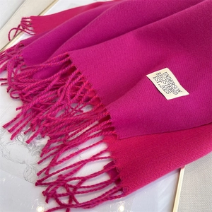 Detailed close-up of rose red cashmere scarf texture with elegant fringe and brand tag