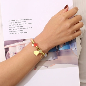 Close-up of colorful beaded bracelet with gold heart pendant worn on wrist over a magazine