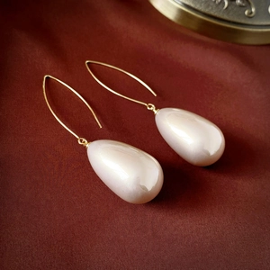 Macro detail of French style waterdrop pearl earrings on elegant dark velvet background