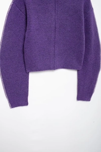 Dettaglio di maglione lavorato a maglia viola con trama spessa e cuciture bianche a contrasto