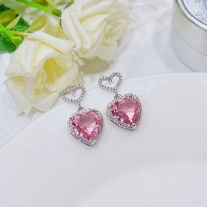 Close-up of pink heart-shaped crystal earrings on white ceramic with rose petals