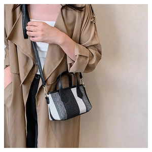 Striped canvas crossbody bag with black leather straps worn over a khaki trench coat