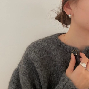 Detail showing minimalist silver spherical earrings and an organic ring on a model