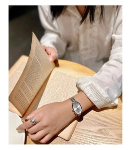 Detail of silver oval vintage watch on woman's wrist while browsing old books