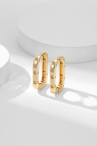 Detailed close-up of rectangular gold earrings with sparkling zircon pave on white studio props