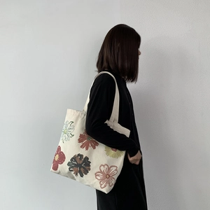 Detail view of colorful floral prints on a cream canvas tote bag worn by a model