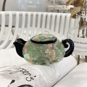 Teapot-shaped acetate hair claw clip with vintage floral marble pattern on magazine