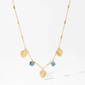 Golden necklace with hollow monstera leaves and blue crystal cubes on a grey background