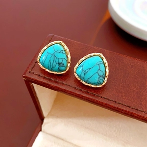 Detail of vintage turquoise triangle stud earrings with gold metal frame on leather
