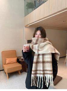 Close-up of beige and brown plaid mohair scarf with tassels worn in a cozy cafe setting